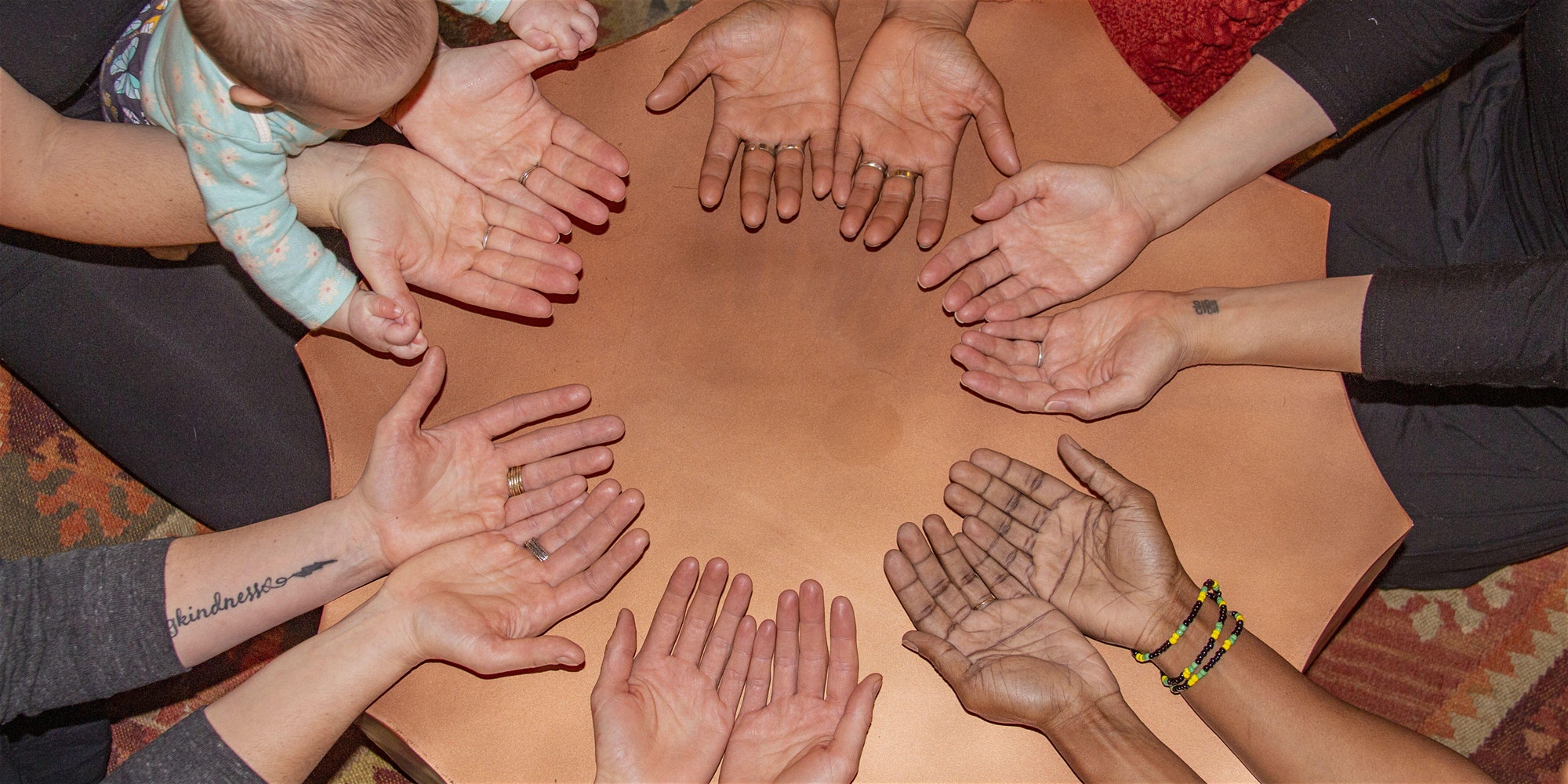 A group of 6 people sit in a circle with their hands in a circle and palms facing up.